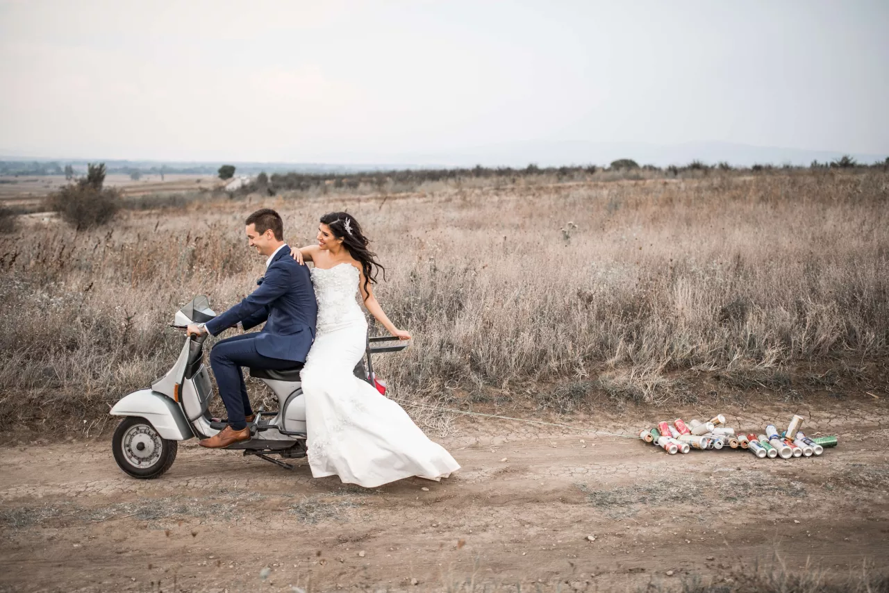 Bride and groom riding moped with cans tied to back
