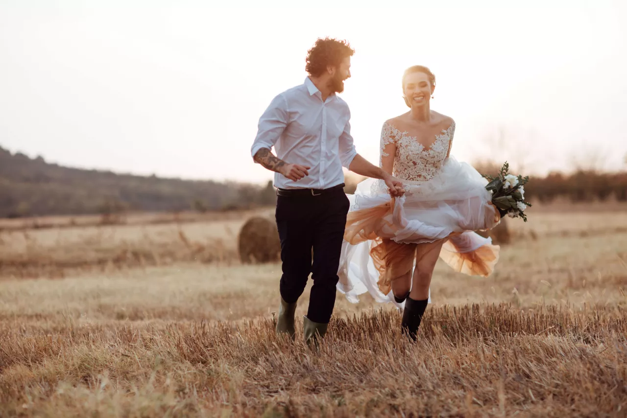 Bride and groom holding hands running through field