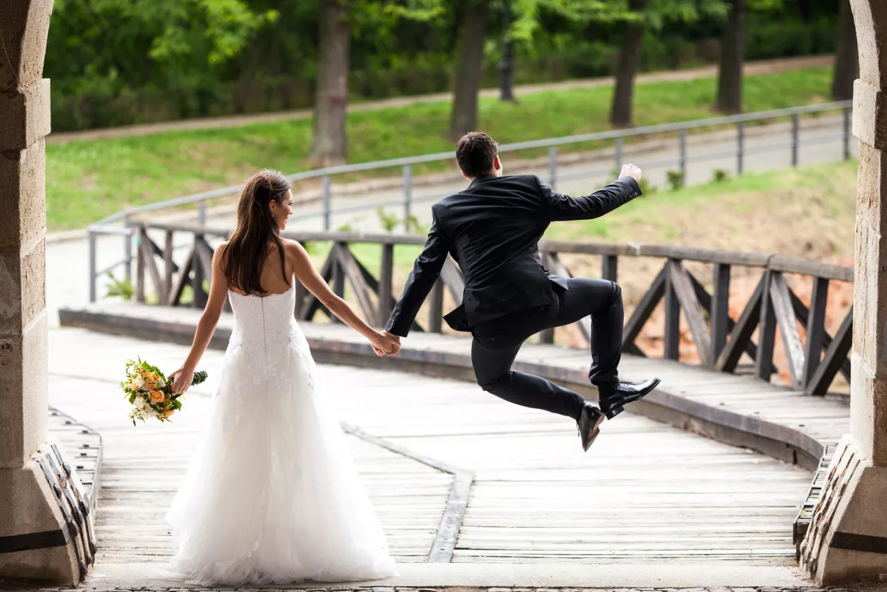 groom jumping in air holding brides hand