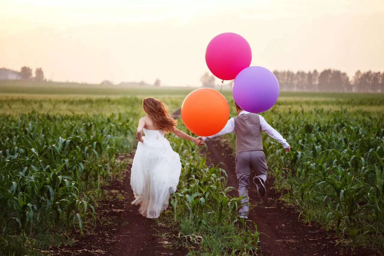 bride and groom running in field with balloons