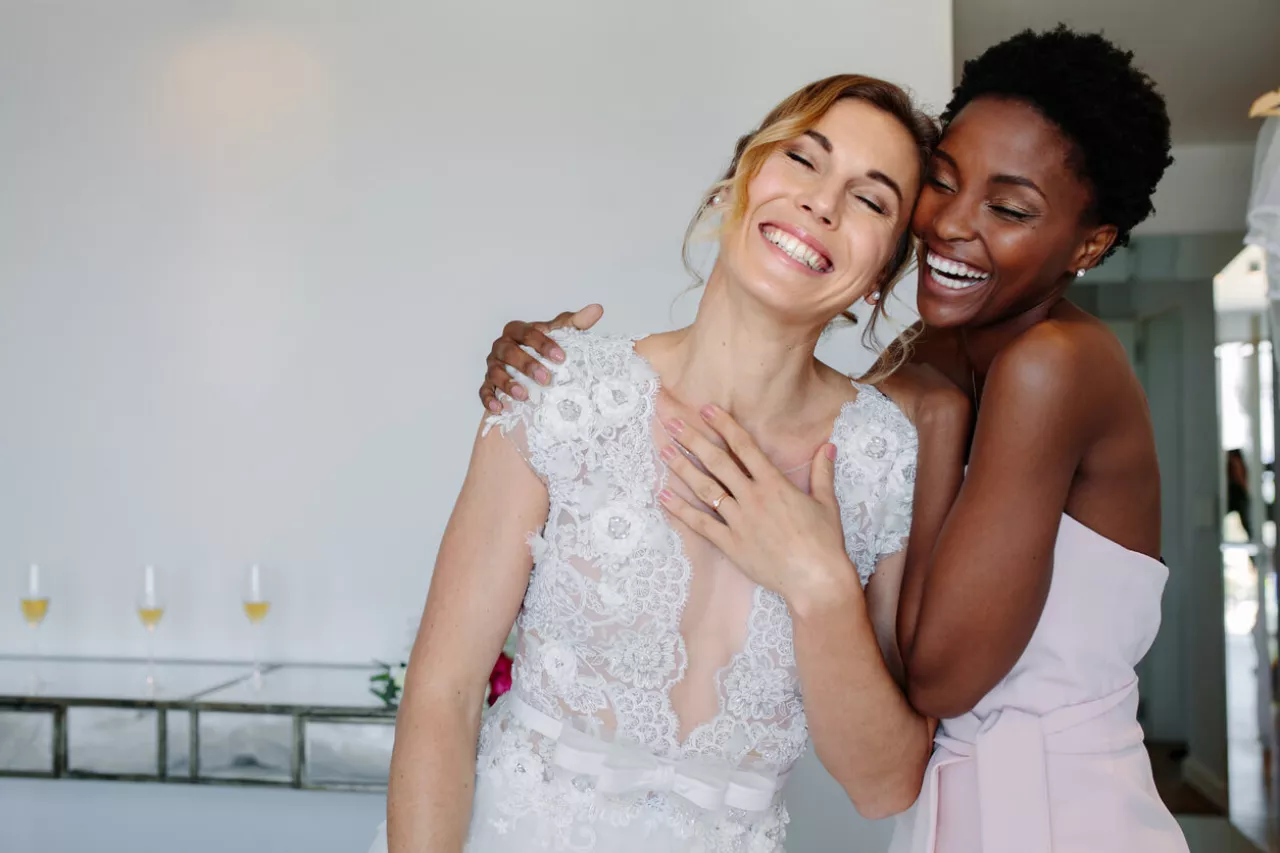 bride and maid of honor hugging and laughing at wedding