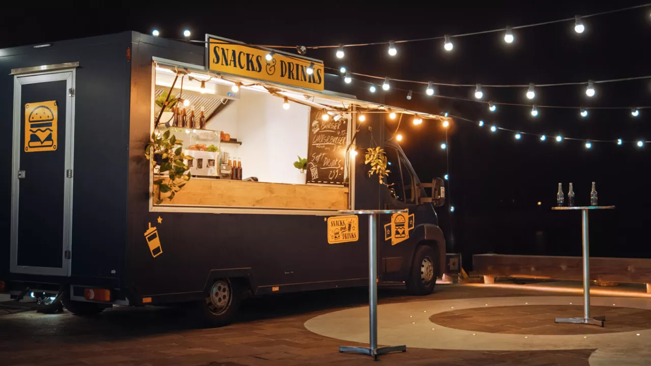 food truck parked outside with string lights and cocktail tables