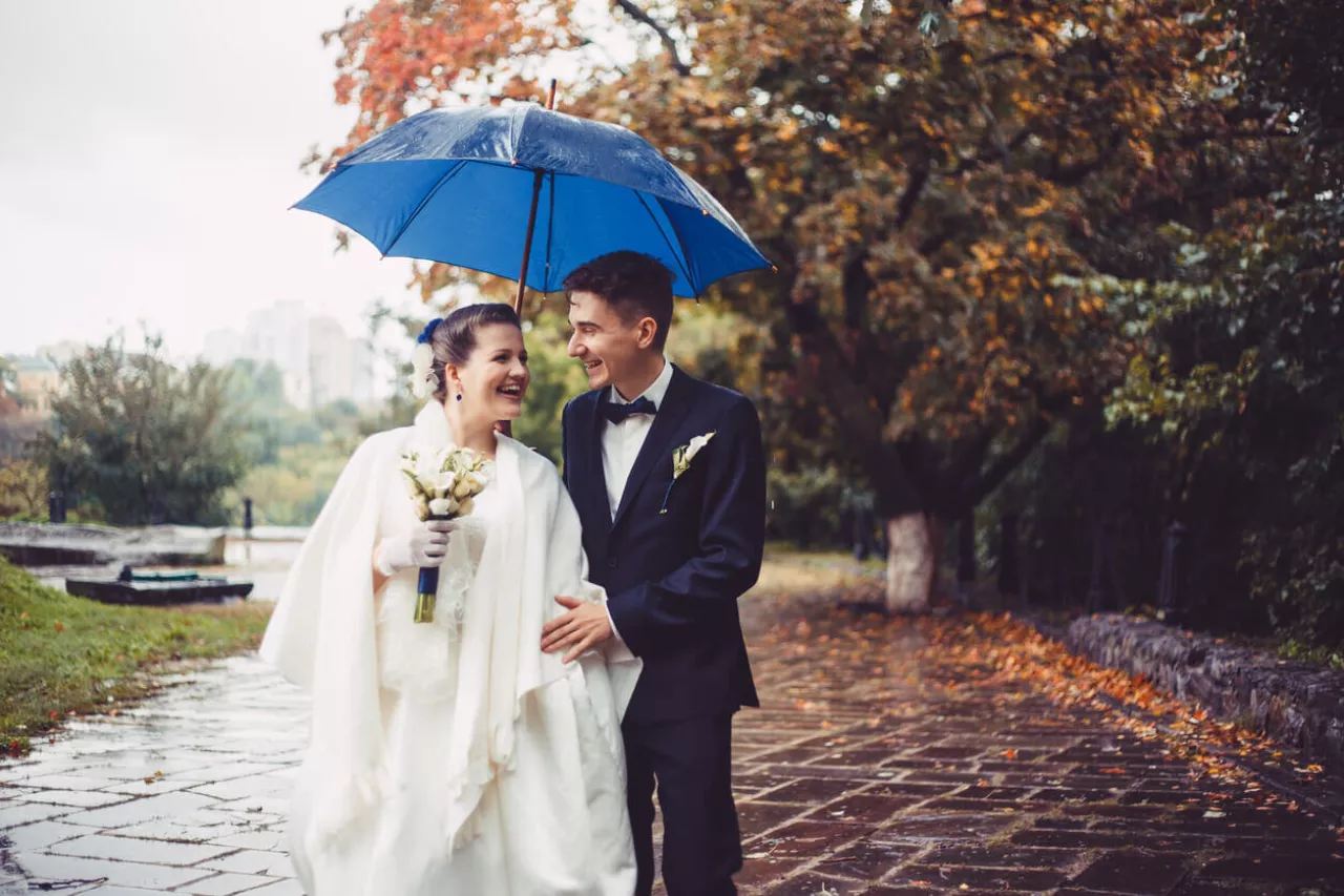 bride and groom smiling under umbrella during rainy wedding day