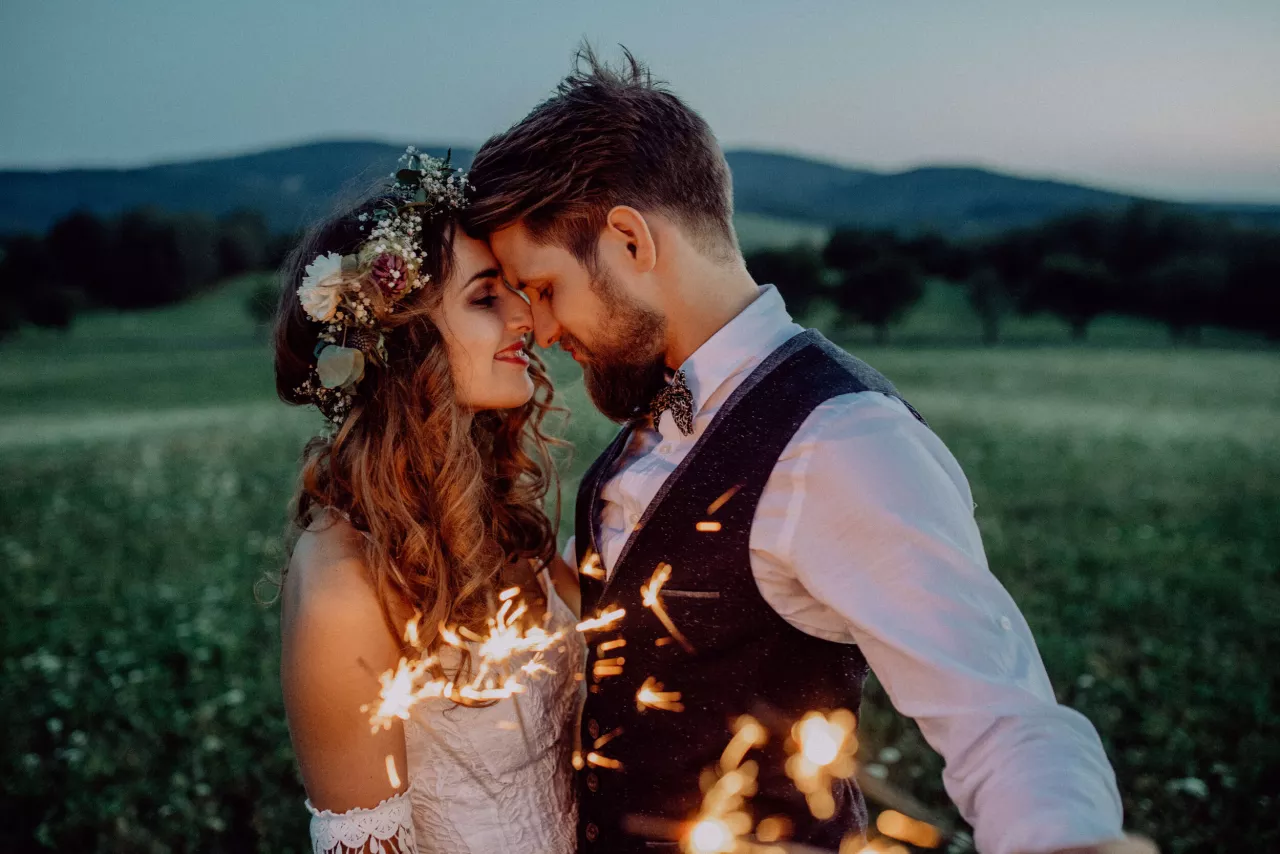 Bride and groom kissing in field holding sparklers